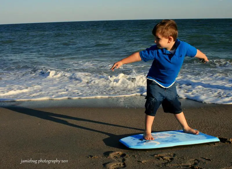 Boy riding a skimboard through shallow surf at Edisto Beach