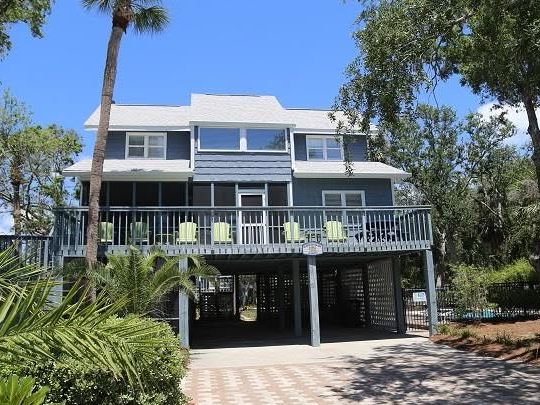 Blue-gray three-story raised rental home among palm trees on Edisto Island